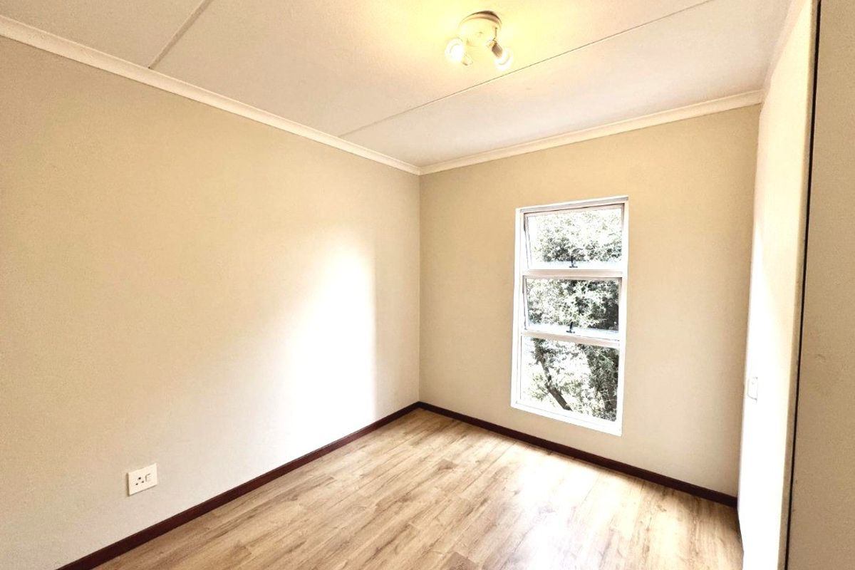 A bright, empty bedroom featuring modern laminate flooring, a built-in cupboard, and a window providing natural light.