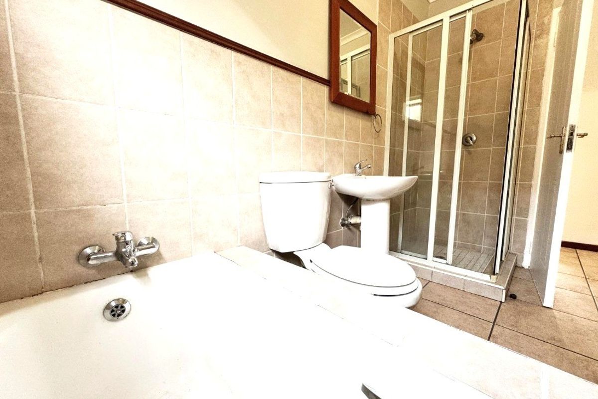 A functional bathroom featuring a bathtub, separate shower enclosure, pedestal basin, and toilet with neutral wall and floor tiling.