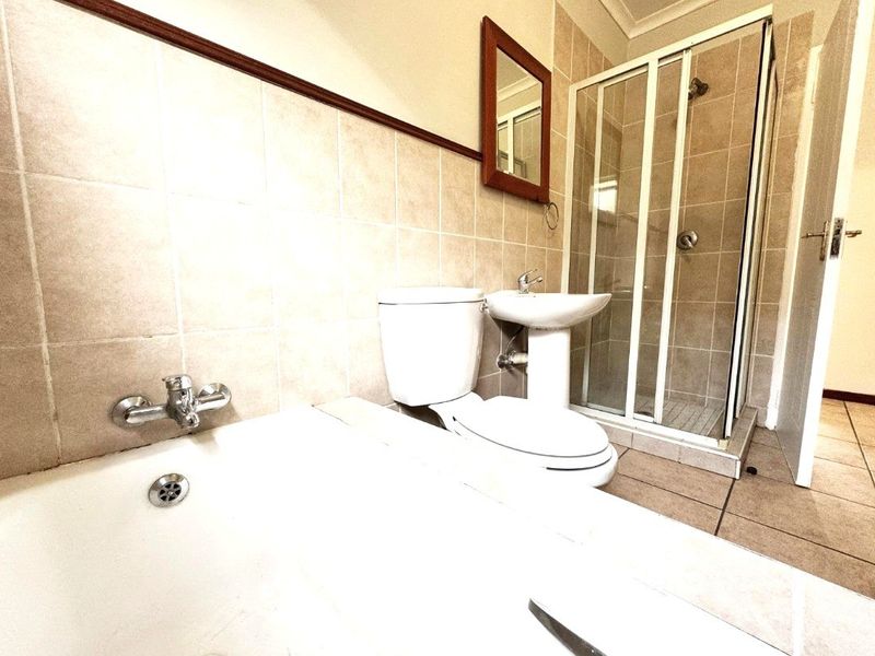 A functional bathroom featuring a bathtub, separate shower enclosure, pedestal basin, and toilet with neutral wall and floor tiling.