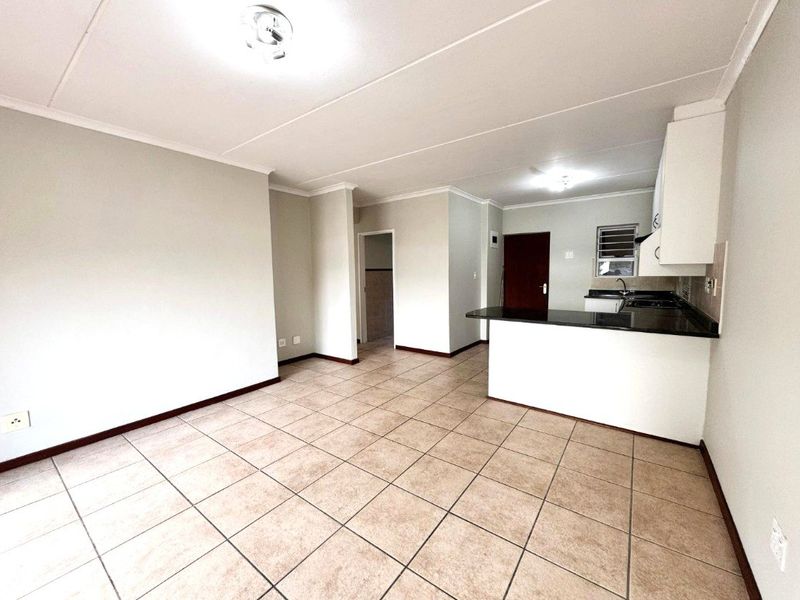 An open-plan living and kitchen area featuring tiled flooring, neutral walls, and a functional kitchen with granite countertops and built-in cabinetry.