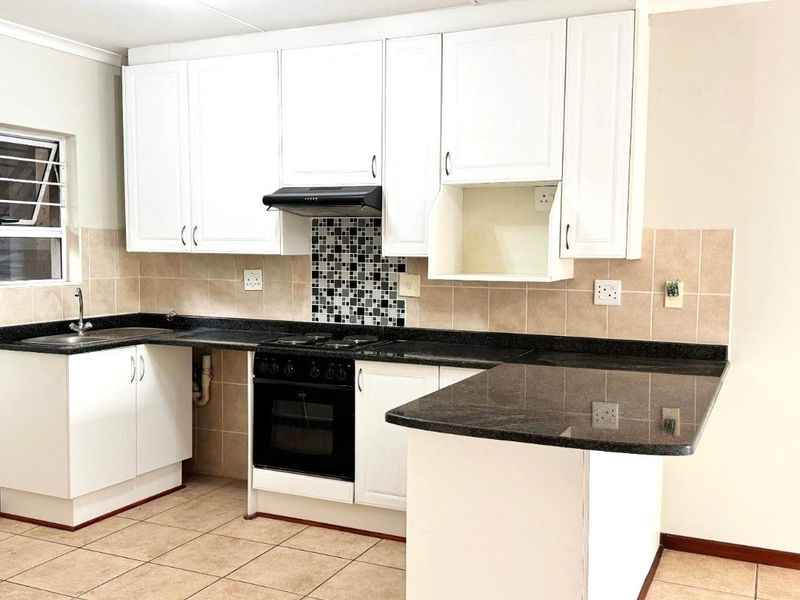 A functional kitchen featuring white cabinetry, granite countertops, a built-in oven with hob, and a tiled backsplash, offering a clean and practical workspace.