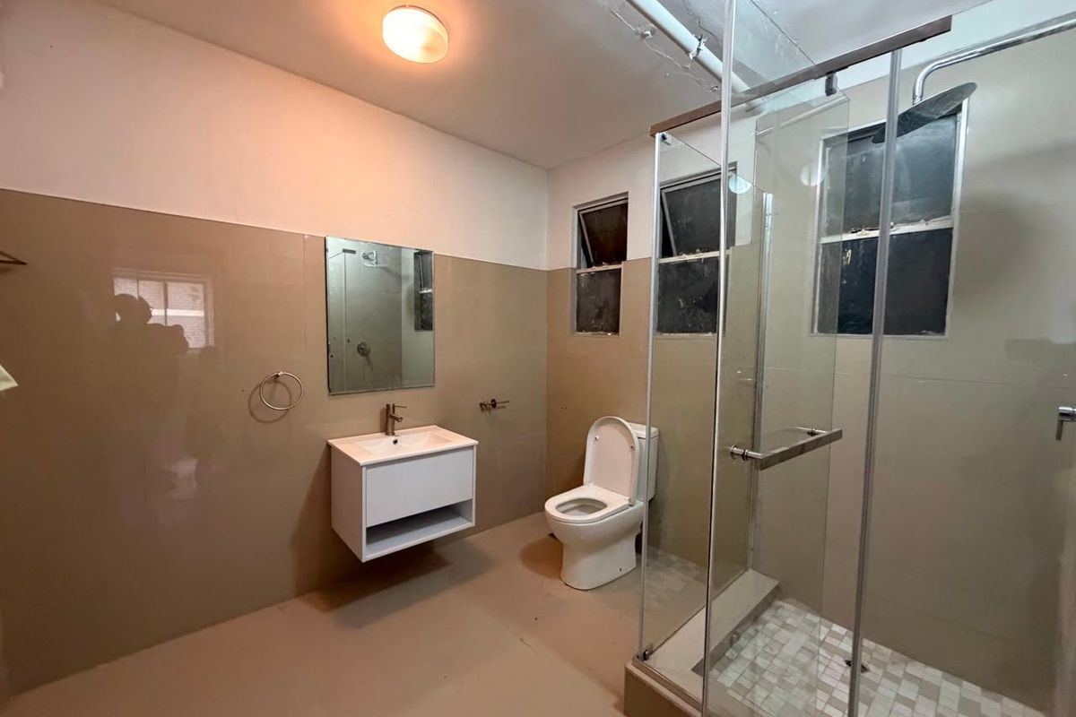 A functional bathroom featuring a wall-mounted vanity, glass-enclosed shower, and neutral wall tiling. The space is clean and ready for personal finishing touches.