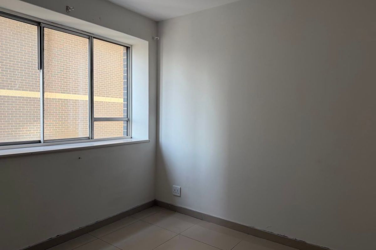An empty bedroom featuring tiled flooring, neutral walls, and an aluminium-framed window, providing a blank canvas for personalization.