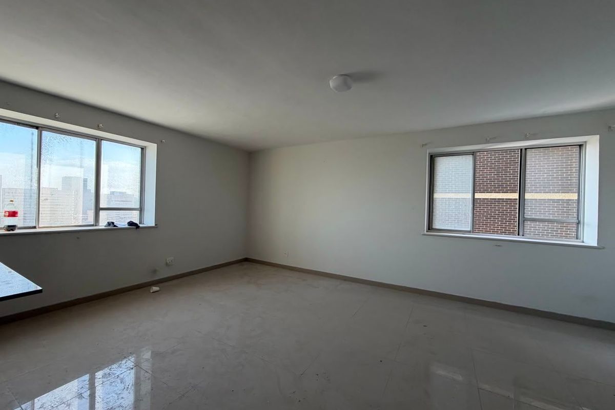A spacious, empty living area featuring neutral tiled flooring and large windows, providing a blank canvas for interior design and personalization.