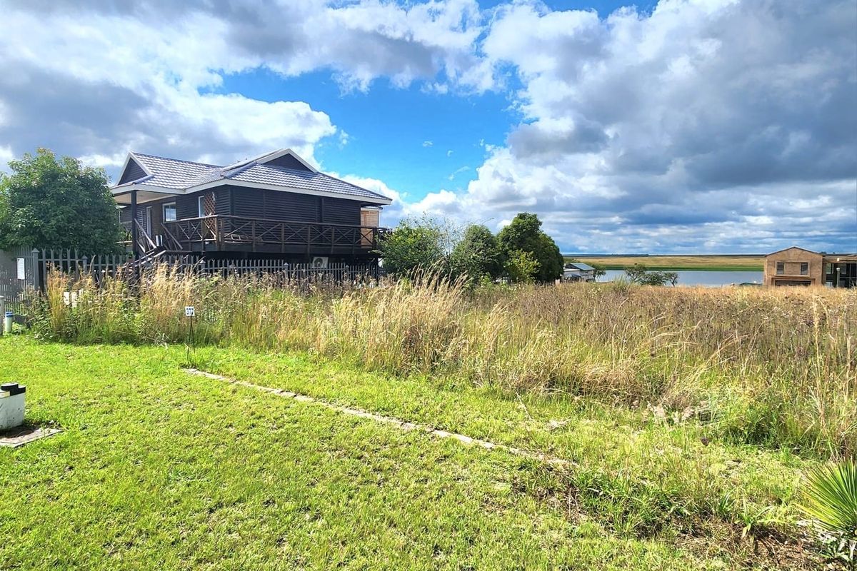 A view of a residential property featuring an elevated timber deck, metal roofing, and a spacious grassed yard with surrounding landscape.