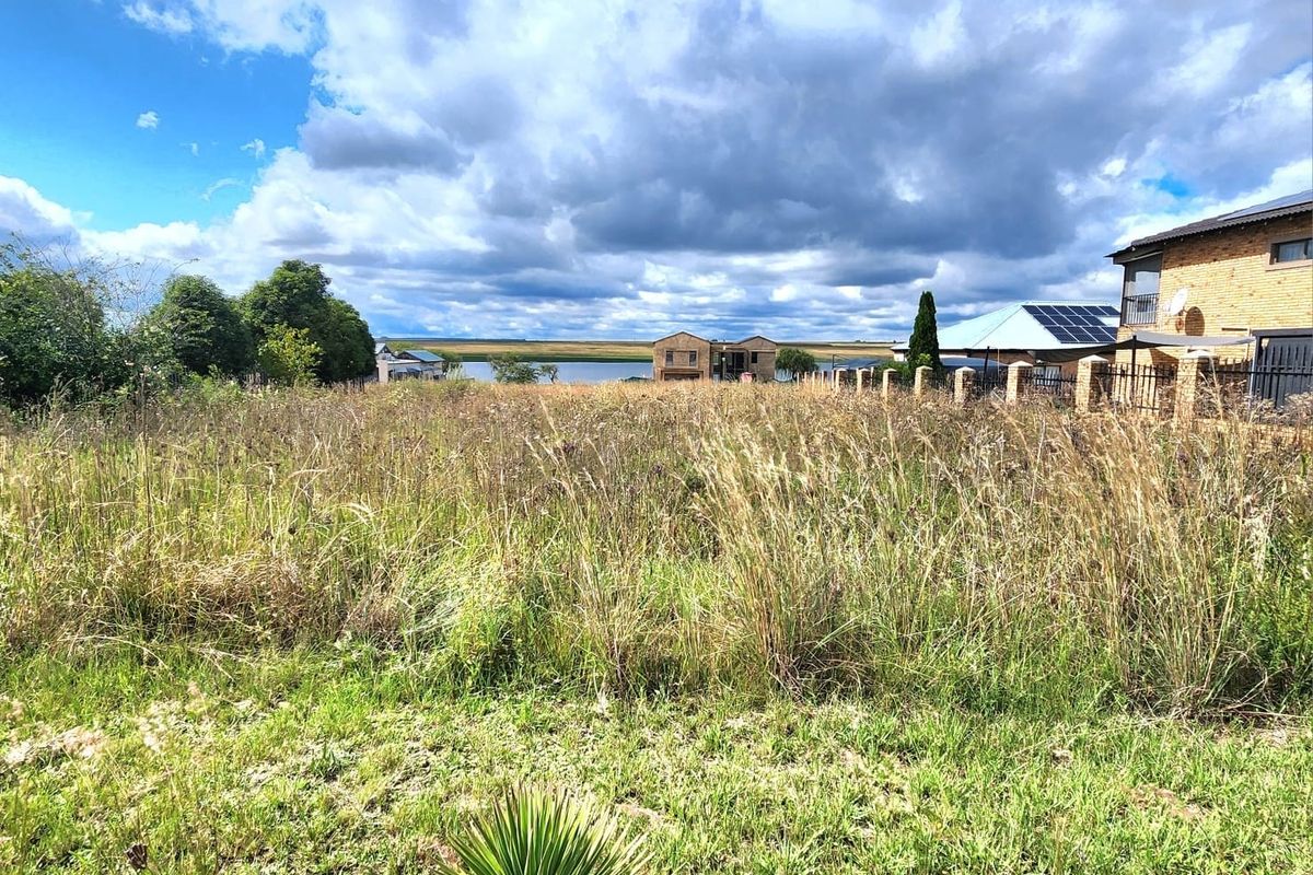 A vacant residential plot featuring natural grass coverage with a view of the surrounding landscape and neighboring properties.