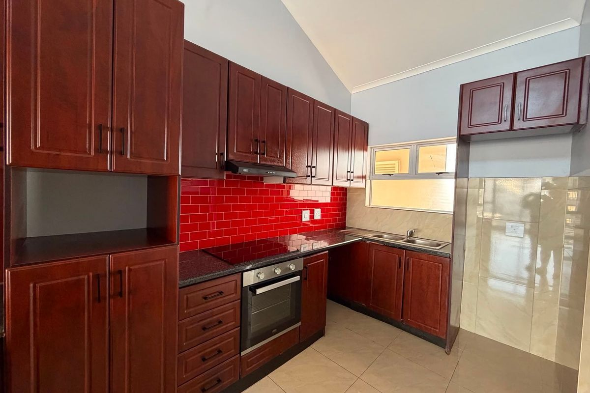 A clean, functional kitchen featuring dark wood cabinetry, granite countertops, a red tiled backsplash, and built-in oven with hob.