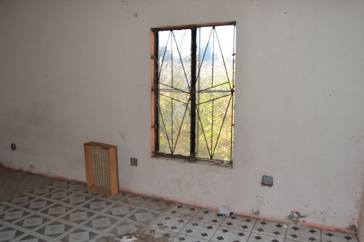 An empty bedroom featuring tiled flooring, a window with security bars, and walls requiring cosmetic repair and repainting.