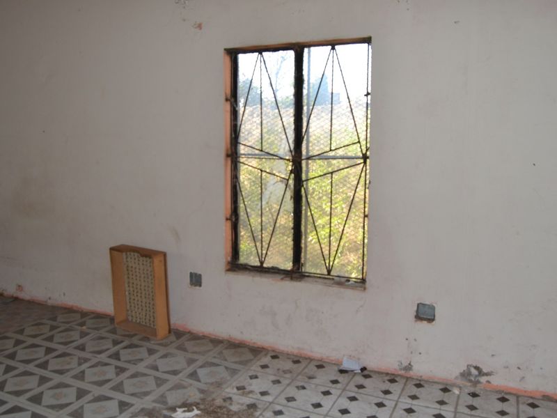 An empty bedroom featuring tiled flooring, a window with security bars, and walls requiring cosmetic repair and repainting.