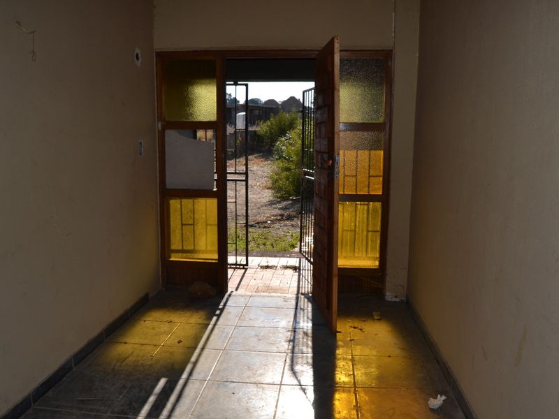 An empty entrance hall featuring tiled flooring and a timber-framed glass door with an integrated security gate leading to the exterior.
