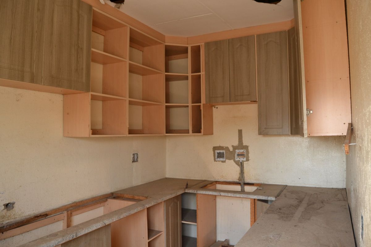 A dilapidated kitchen space featuring built-in cabinetry, countertops, and a sink, requiring significant renovation and repair to restore functionality.