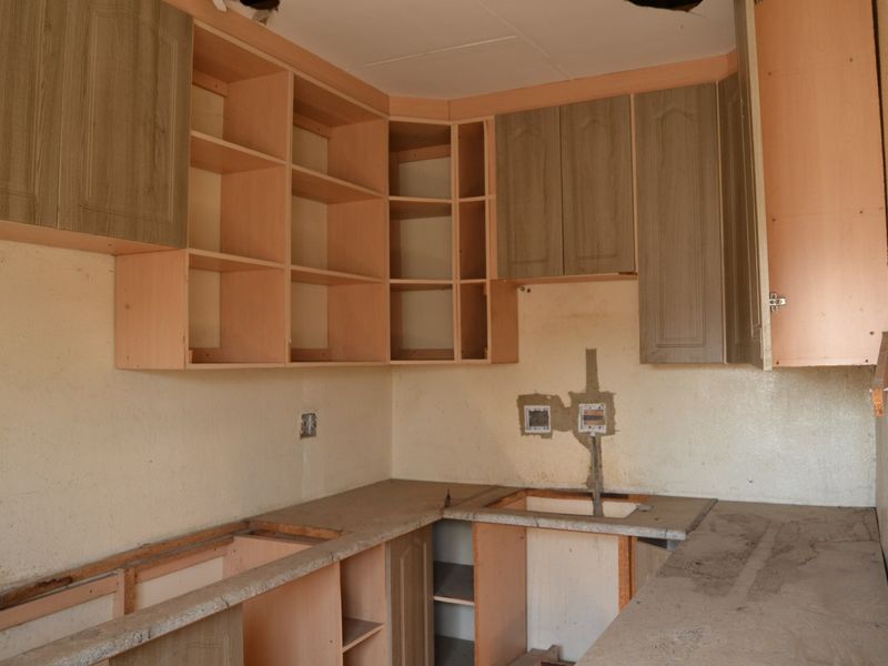 A dilapidated kitchen space featuring built-in cabinetry, countertops, and a sink, requiring significant renovation and repair to restore functionality.