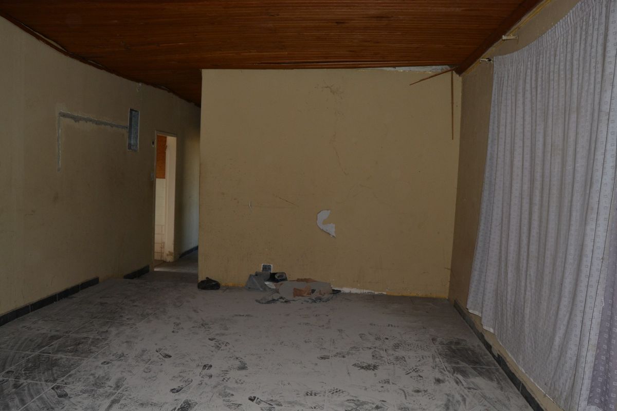 An empty living room featuring a timber ceiling and tiled flooring, currently requiring significant cosmetic repairs and refurbishment to restore its condition.