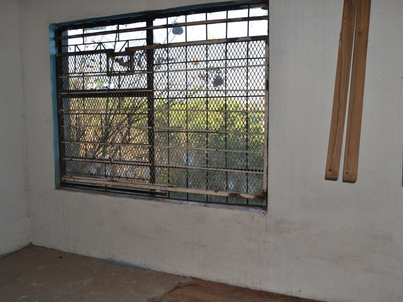 An empty bedroom featuring a window with security bars, requiring cosmetic updates and wall repairs to improve the overall condition.