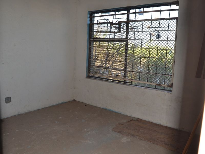 An empty bedroom featuring a window with security bars, requiring cosmetic updates and flooring repairs to restore its condition.