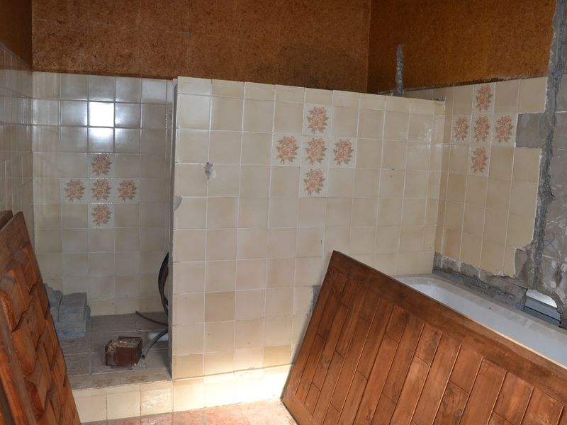 A bathroom in a state of renovation, featuring a built-in bathtub and partially tiled walls with visible masonry and missing tile sections.