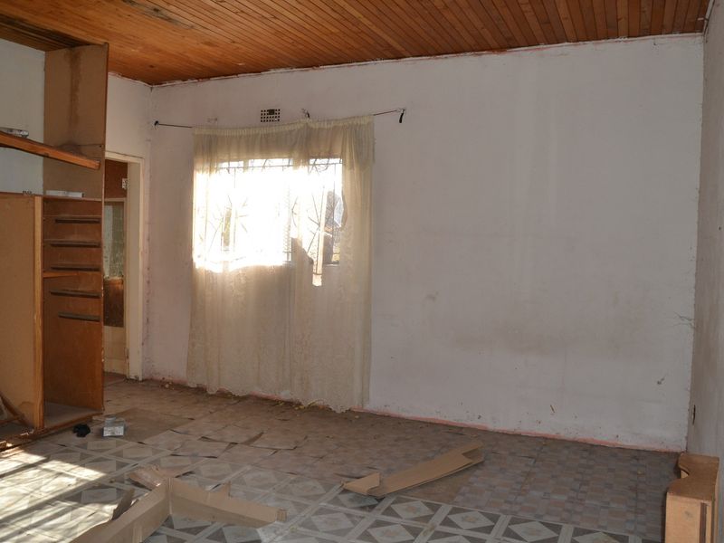 A vacant bedroom featuring a timber ceiling, built-in storage, and tiled flooring, requiring significant cosmetic renovation and repair to restore its condition.