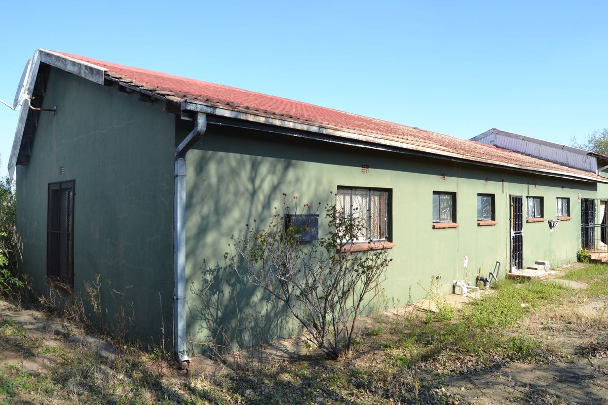 Rear exterior view of a single-story house featuring a corrugated metal roof, security bars on windows, and visible exterior wall plaster cracking.