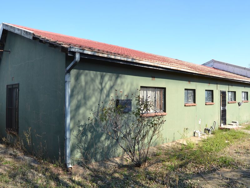 Rear exterior view of a single-story house featuring a corrugated metal roof, security bars on windows, and visible exterior wall plaster cracking.