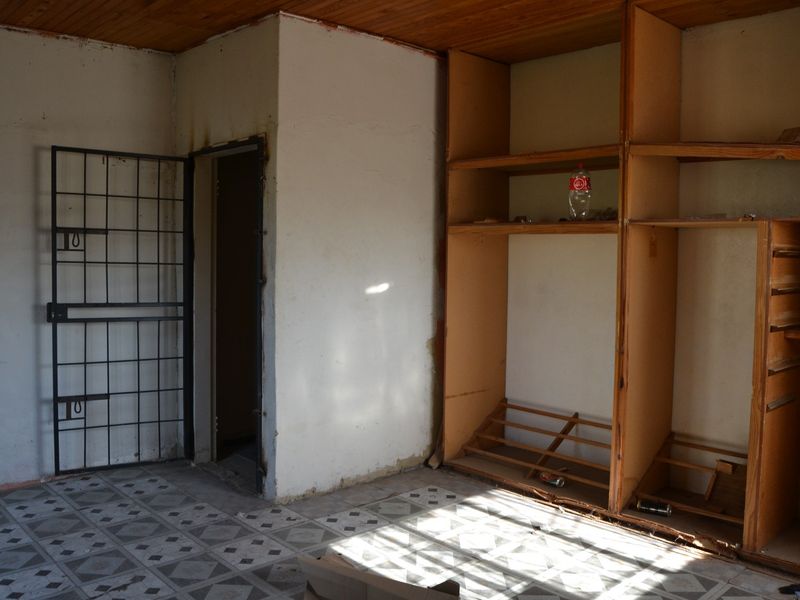 An empty bedroom featuring built-in wooden shelving, a security gate, tiled flooring, and a timber ceiling, requiring cosmetic updates.