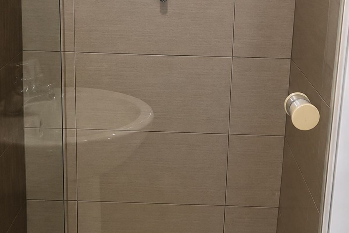 A clean, functional shower enclosure featuring neutral wall tiles, a glass screen, and a louver window for ventilation.