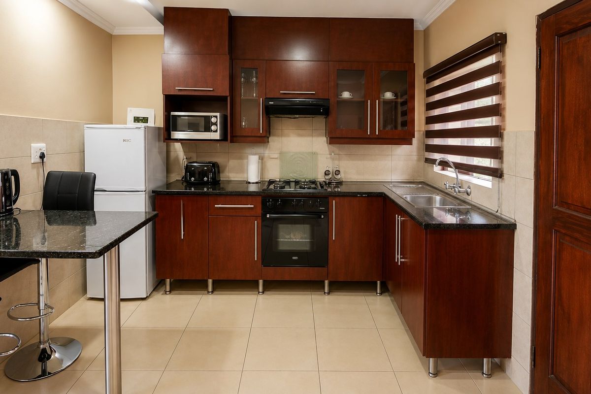 A well-maintained kitchen featuring dark wood cabinetry, granite countertops, built-in oven with gas hob, and tiled flooring.