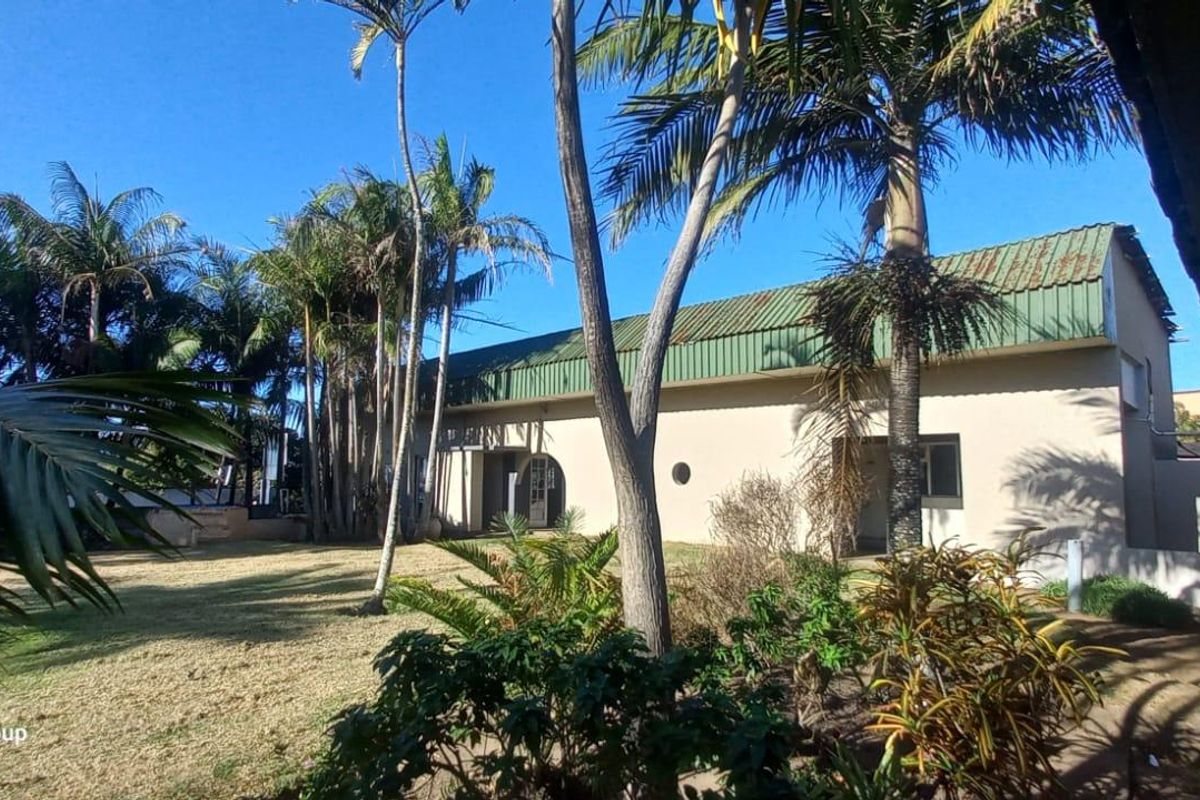 Rear view of the commercial property featuring a landscaped garden, mature palm trees, and a covered walkway with brick pillars.