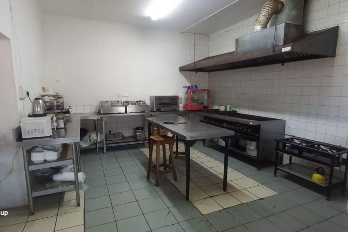 Commercial kitchen space featuring stainless steel prep surfaces, an industrial extractor hood, tiled wall splashbacks, and essential fire safety equipment.