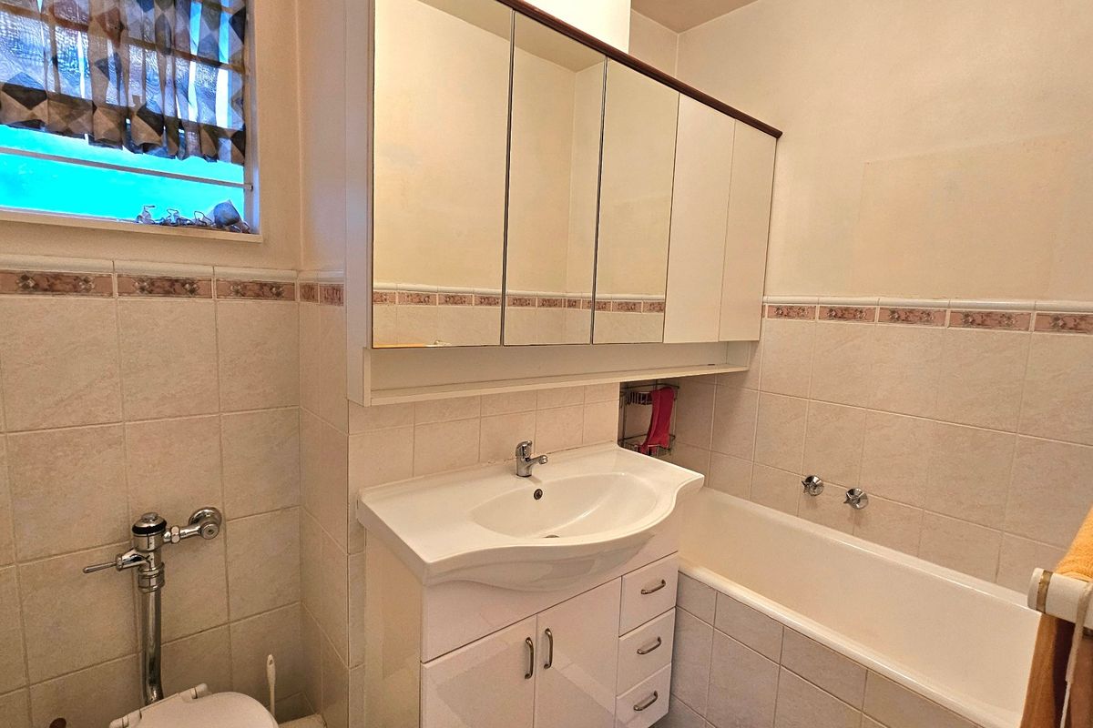 A functional bathroom featuring a vanity with integrated basin, mirrored medicine cabinet, bathtub, and tiled wall finishes.