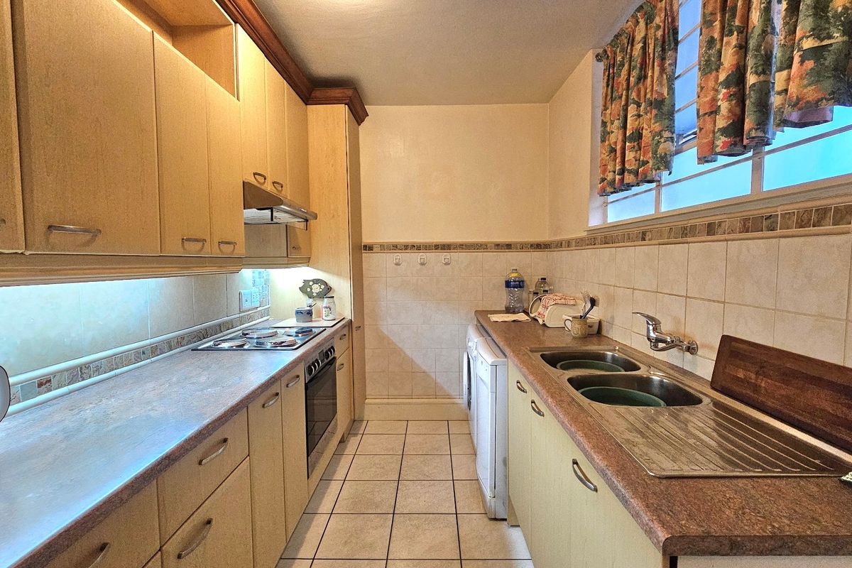 A functional galley-style kitchen featuring laminate countertops, built-in cabinetry, a stainless steel double sink, and integrated cooking appliances.