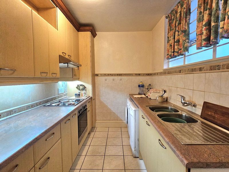 A functional galley-style kitchen featuring laminate countertops, built-in cabinetry, a stainless steel double sink, and integrated cooking appliances.