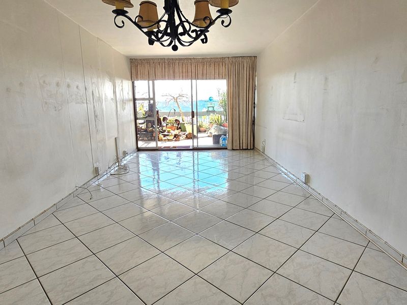 An empty living room featuring tiled flooring, a central light fixture, and sliding glass doors leading to an outdoor balcony area.
