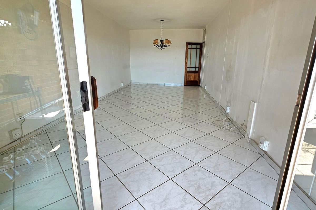 An empty, open-plan living area featuring tiled flooring, a sliding glass door entrance, and a traditional timber door, requiring cosmetic updates to walls and finishes.