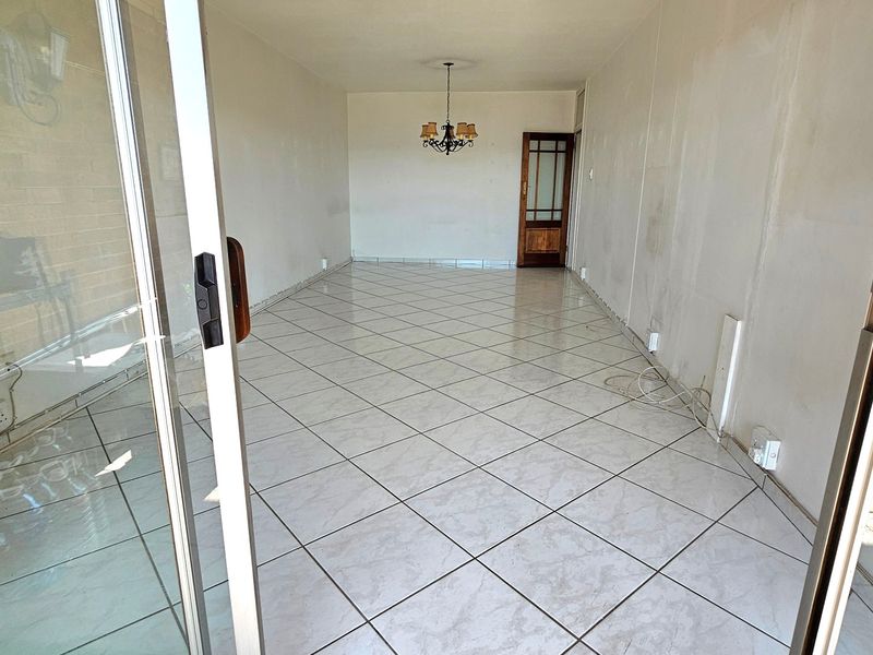 An empty, open-plan living area featuring tiled flooring, a sliding glass door entrance, and a traditional timber door, requiring cosmetic updates to walls and finishes.