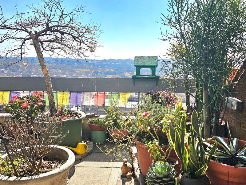 A balcony featuring paved flooring, a metal railing, and a brick wall, offering an elevated view of the surrounding landscape.