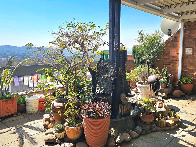 A spacious covered balcony featuring paved flooring, brick wall accents, and expansive views, providing a pleasant outdoor area for relaxation.