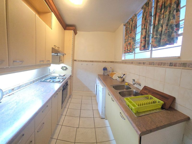 A functional galley-style kitchen featuring built-in cabinetry, laminate countertops, a stainless steel double sink, and integrated cooking appliances with tiled flooring.