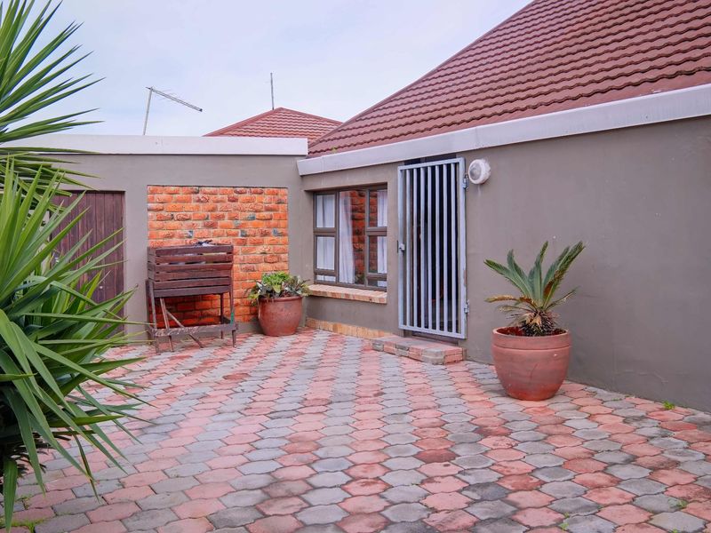 A paved rear courtyard area featuring a brick accent wall, security gate access, and a tiled roof structure.