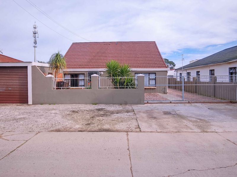 Front elevation of a single-story house featuring a tiled roof, perimeter wall with metal gate, and a private garage.