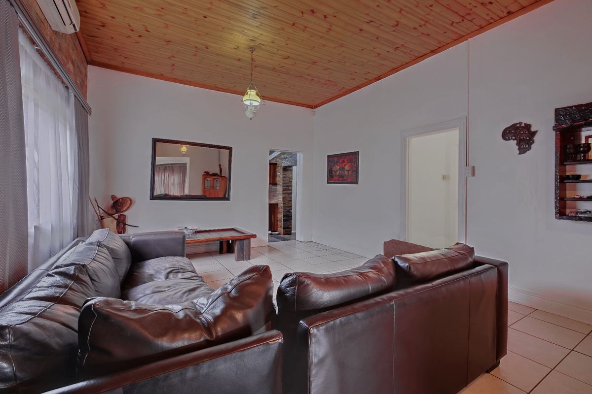A living room featuring a timber tongue and groove ceiling, ceramic tiled flooring, and an air conditioning unit, with access to adjacent rooms.
