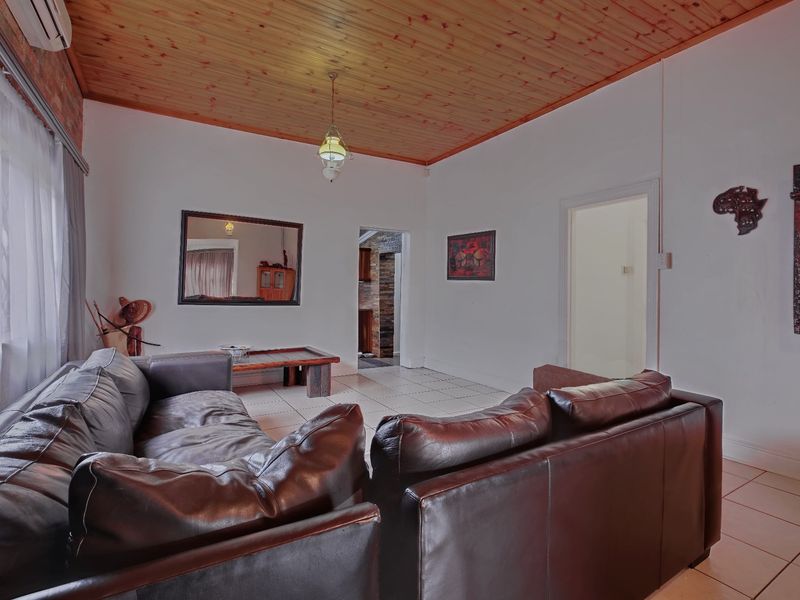 A living room featuring a timber tongue and groove ceiling, ceramic tiled flooring, and an air conditioning unit, with access to adjacent rooms.