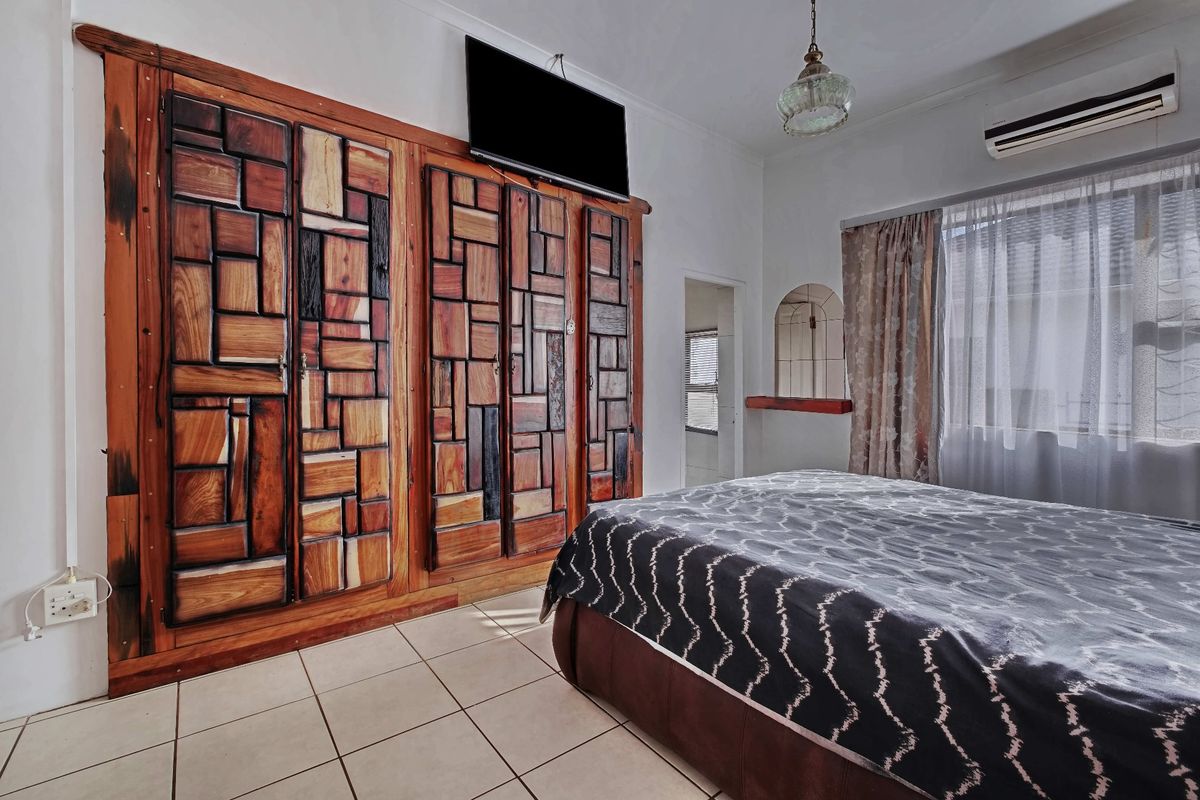 A bedroom featuring tiled flooring, a large custom-built wooden wardrobe, a wall-mounted air conditioning unit, and a decorative arched wall niche.