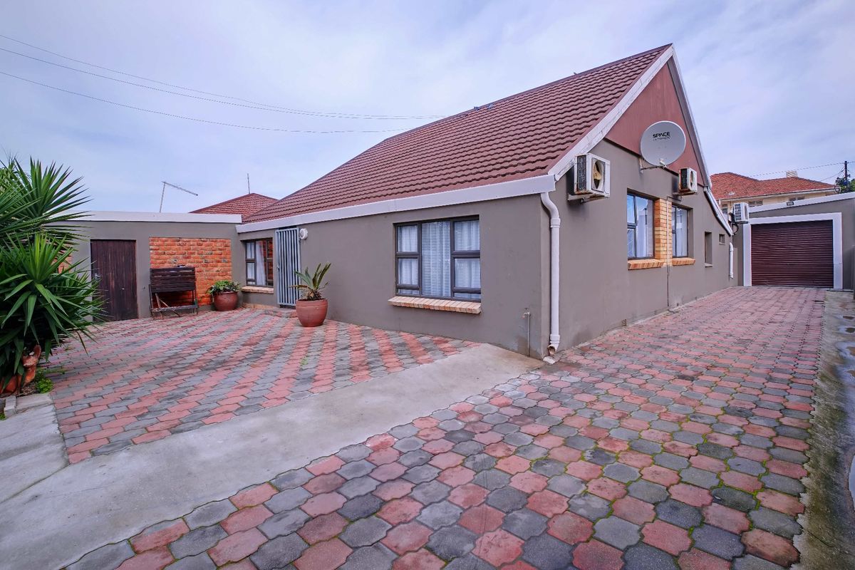 Rear exterior view of the house featuring a paved courtyard, tiled roof, and mounted air conditioning units.