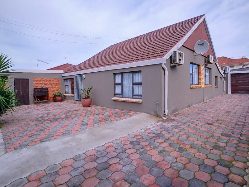 Rear exterior view of the house featuring a paved courtyard, tiled roof, and mounted air conditioning units.