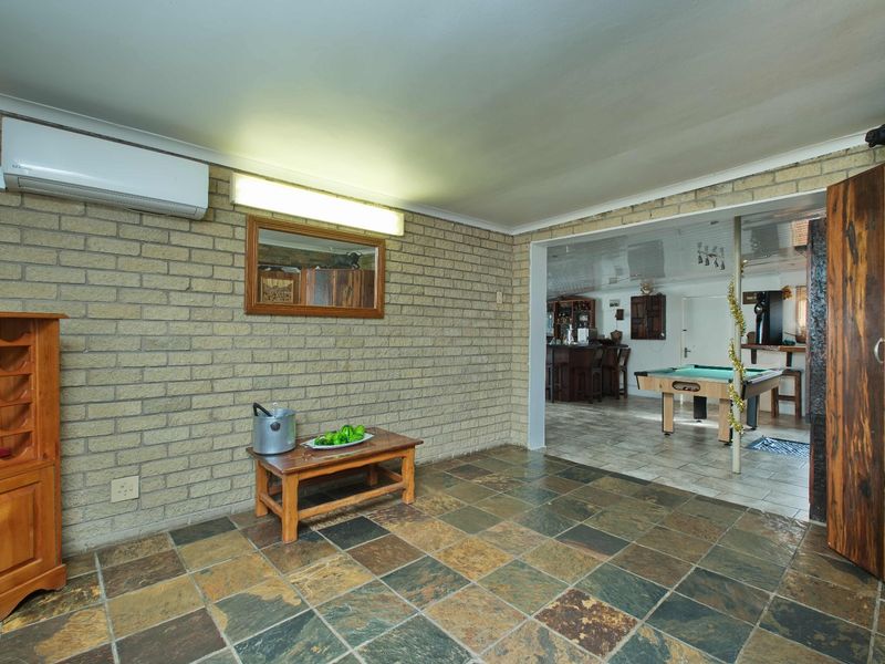 A living area featuring exposed brick walls, slate tile flooring, and a wall-mounted air conditioning unit, with an adjacent room visible through the doorway.