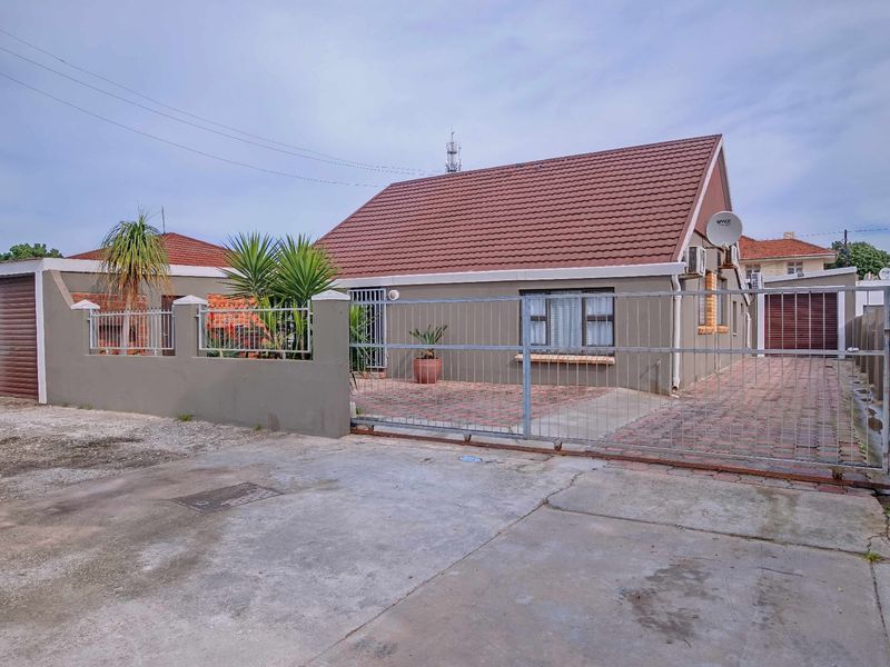Front exterior view of a single-story house featuring a tiled roof, paved driveway, perimeter wall with sliding gate, and an attached garage.