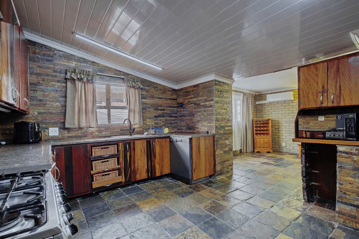 A rustic kitchen featuring stone-clad walls, slate flooring, wooden cabinetry, and built-in appliances, offering a warm and textured aesthetic.