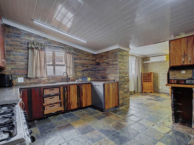 A rustic kitchen featuring stone-clad walls, slate flooring, wooden cabinetry, and built-in appliances, offering a warm and textured aesthetic.