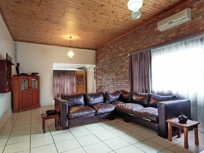 A living room featuring a distinctive exposed brick wall, timber ceiling, and neutral ceramic floor tiles, equipped with a wall-mounted air conditioning unit.