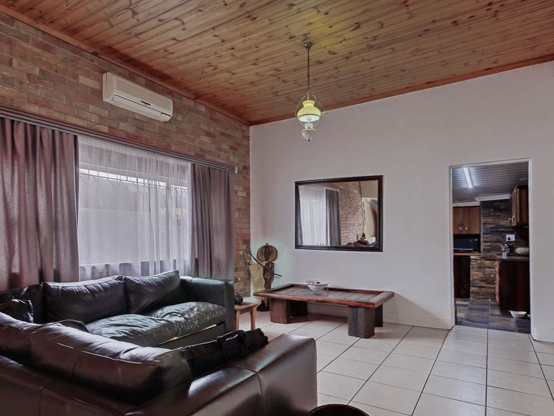 Spacious living room featuring an exposed brick feature wall, timber ceiling, and tiled flooring, with direct access to the kitchen area.
